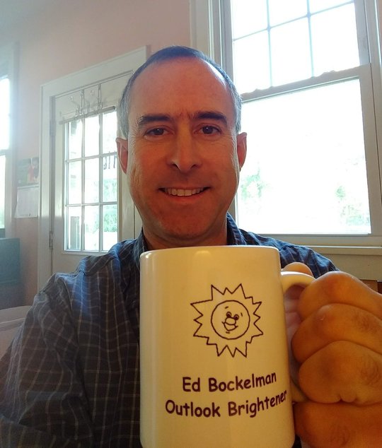 The website author holding a mug with logo and slogan on the side